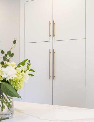 A white kitchen with white cabinets and a vase of flowers.