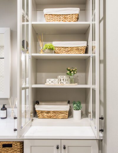 A white bathroom with a glass cabinet and baskets.