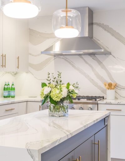 A modern kitchen with marble counter tops and pendant lights.