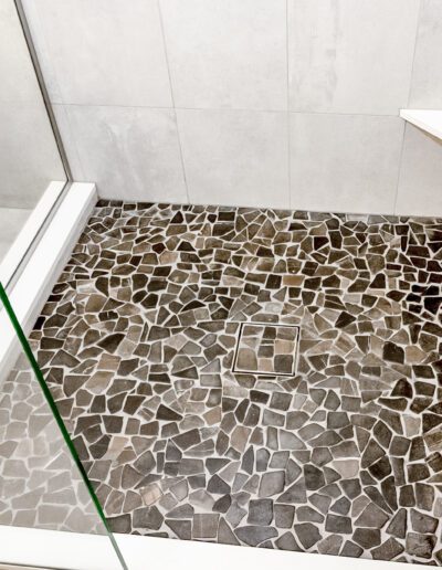 A bathroom with a glass shower stall and tiled floor.