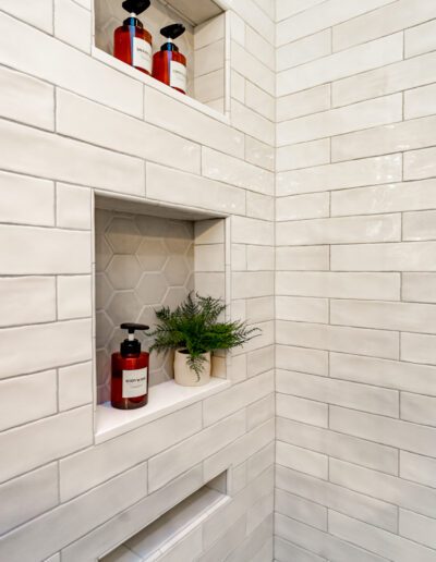 A white tiled shower with shelves and plants.