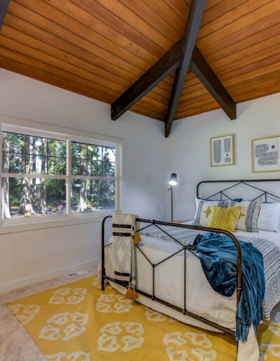 A bedroom with wooden ceilings and a yellow rug.